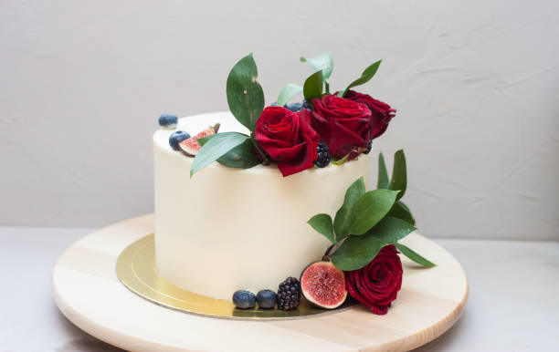 Elegant wedding cake decorated with fresh red roses, green leaves, figs and blueberry. Plain grey background. Elegant wedding cake decorated with fresh red roses, green leaves, figs and blueberry. Plain background. white wedding cake red roses stock pictures, royalty-free photos & images