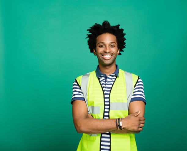 Portrait of friendly man wearing reflective waistcoat Portrait of happy afro american young man wearing striped polo shirt and yellow safety waistcoat, smiling at camera. Studio shot on green background. waistcoat stock pictures, royalty-free photos & images