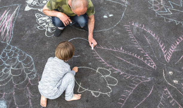 Young boy doodling on asphalt with his father