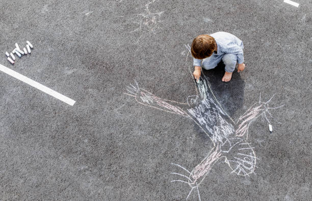 Young boy doodling the asphalt with a chalk