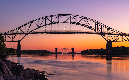 The Bourne Bridge in Bourne, Massachusetts connects Cape Cod with the mainland over the Cape Cod Canal. The tidal change at the canal occurs every six hours or so. This photo was taken approximately one hour after the high tide at 8:43 pm on June 14, 2020.  The architectural structure seen under the bridge at the center is the Cape Cod Canal Railroad Bridge.