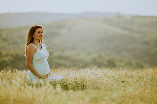 Young pregnant woman in white dress in the summer field