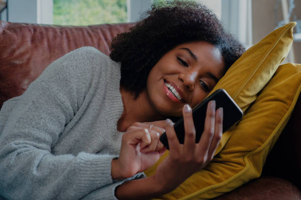 istock Beautiful mixed race woman texting on smart phone while lying on the sofa at home 1249852490