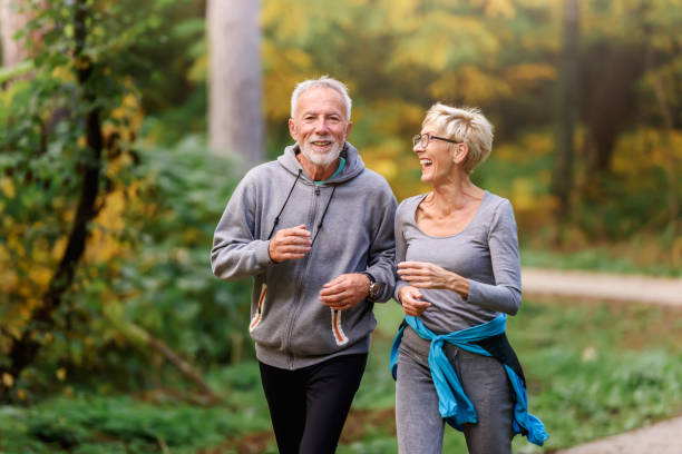 coppia senior sorridente che fa jogging nel parco - anziani attivi foto e immagini stock