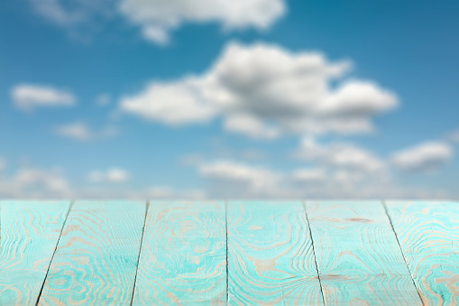 Blank natural wooden blue table against blurred background of blue cloudy sky for present product and other things, copy space. Can be used for your creativity.