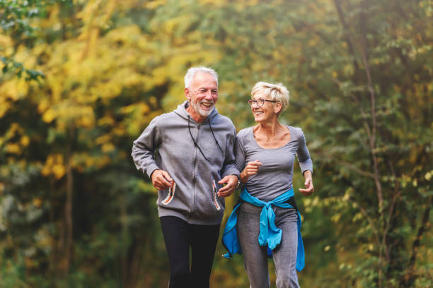 älteres paar im park joggen lächelnd - senior couple stock-fotos und bilder