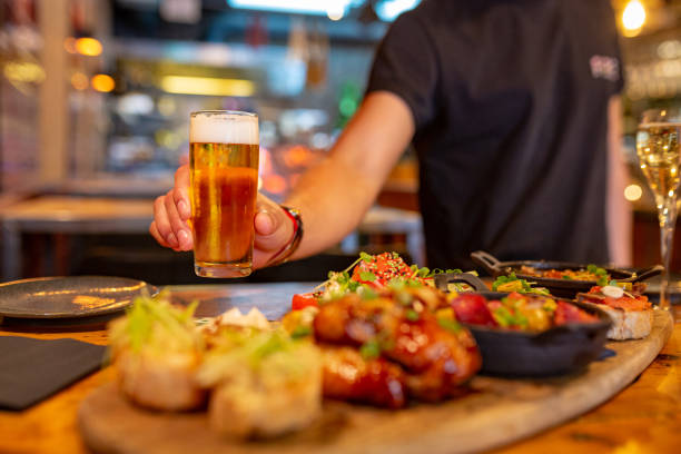 camarero sirviendo cerveza en un restaurante español con una mesa llena de tapas - salad food beer restaurant fotografías e imágenes de stock