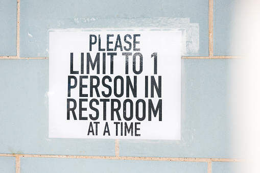 A white sign with black lettering limiting bathroom occupancy during the reopening of businesses during the coronavirus epidemic.