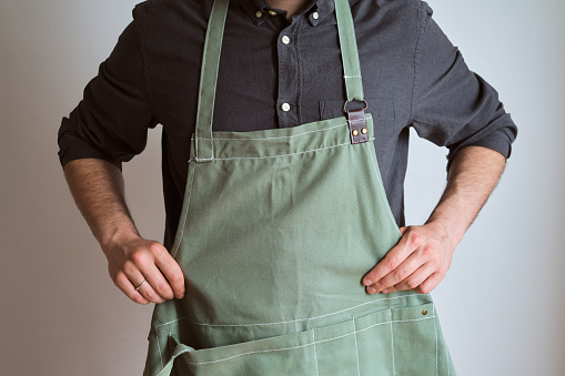 A man in a kitchen apron. Chef work in the cuisine. Cook in uniform, protection apparel. Job in food service. Professional culinary. Green fabric apron, casual stylish clothing. Handsome baker posing in workplace