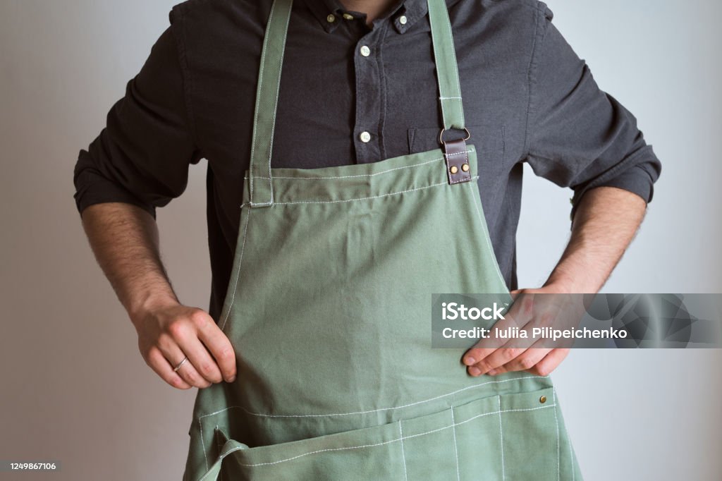 A man in a kitchen apron. Chef work in the cuisine. Cook in uniform, protection apparel. Job in food service. Professional culinary. Green fabric apron, casual stylish clothing. Handsome baker posing in workplace Apron Stock Photo