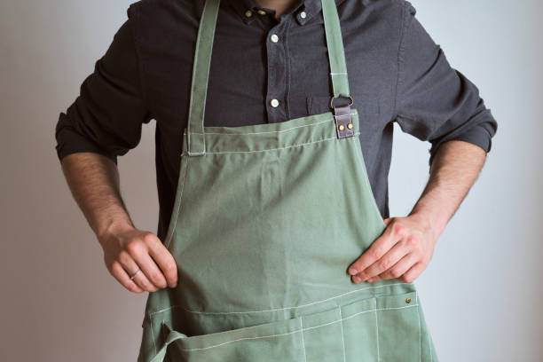 A man in a kitchen apron. Chef work in the cuisine. Cook in uniform, protection apparel. Job in food service. Professional culinary. Green fabric apron, casual stylish clothing. Handsome baker posing in workplace stock photo