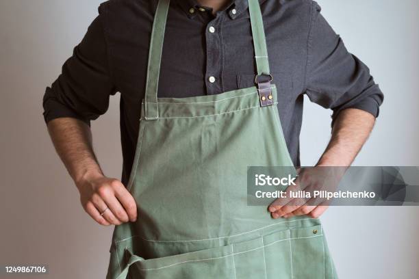 A Man In A Kitchen Apron Chef Work In The Cuisine Cook In Uniform Protection Apparel Job In Food Service Professional Culinary Green Fabric Apron Casual Stylish Clothing Handsome Baker Posing In Workplace Stock Photo - Download Image Now
