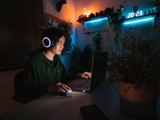 giovane donna asiatica che gioca ai giochi online sul computer portatile di notte. - addiction internet computer working late foto e immagini stock