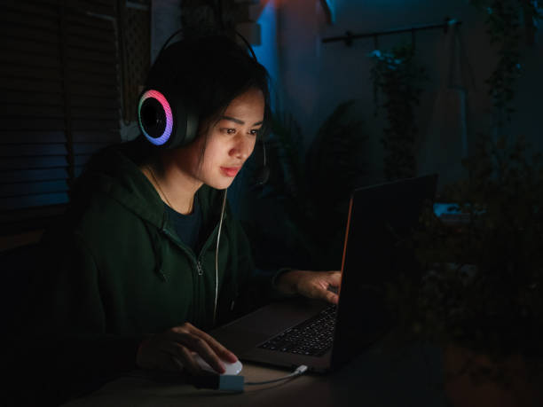 giovane donna asiatica che gioca ai giochi online sul computer portatile di notte. - addiction internet computer working late foto e immagini stock