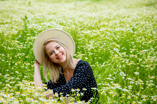 Blonde woman in black dress sitting in countryside chamomiles flowers field