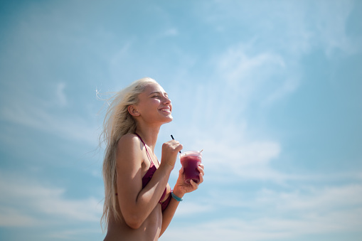 Charming caucasian tanned blond woman drinking refreshment on a beach on beautiful sunny summer day.