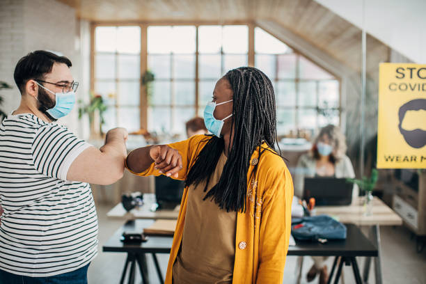 istock Man and woman with protective masks greeting with elbows in office 1249876291