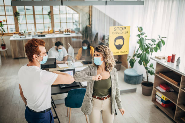 istock Man and woman with protective masks greeting with elbows in office 1249876303
