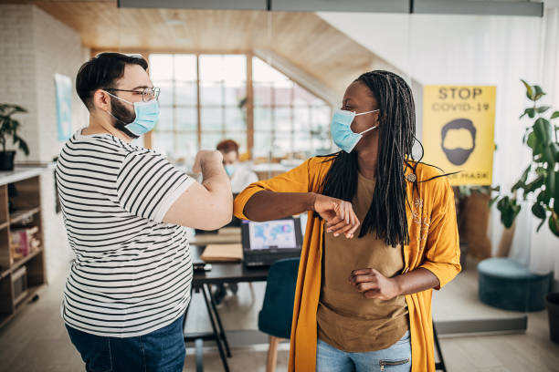 istock Man and woman with protective masks greeting with elbows in office 1249876334