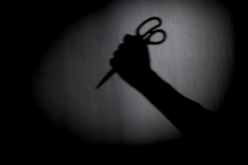 man with scissors silhouette over dark wall. black and white photo can be used for illustrating horror and violence attack. crime concept. simple. selective focus. blurred.