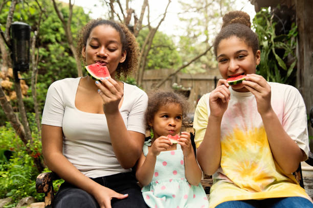 istock Mixed-race sisters eating watermelon in backyard. 1249878114
