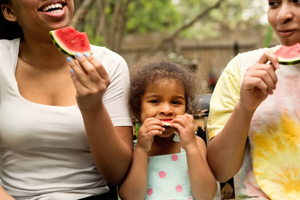 istock Mixed-race sisters eating watermelon in backyard. 1249878659