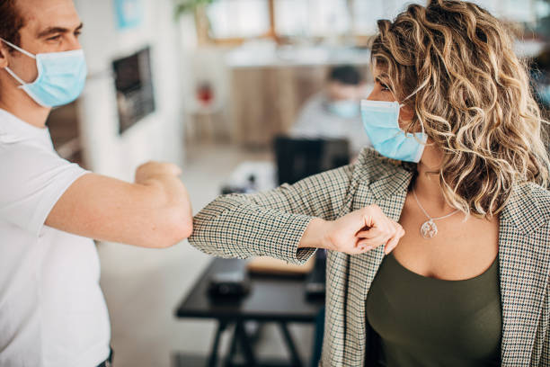 istock Man and woman with protective masks greeting with elbows in office 1249878953