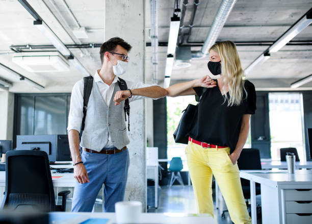 istock Young people with face masks back at work in office after lockdown, greeting. 1249879242