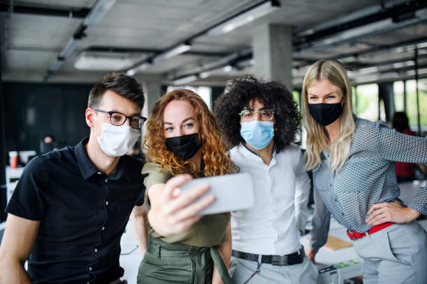 istock Young people with face masks back at work in office after lockdown, taking selfie. 1249879778