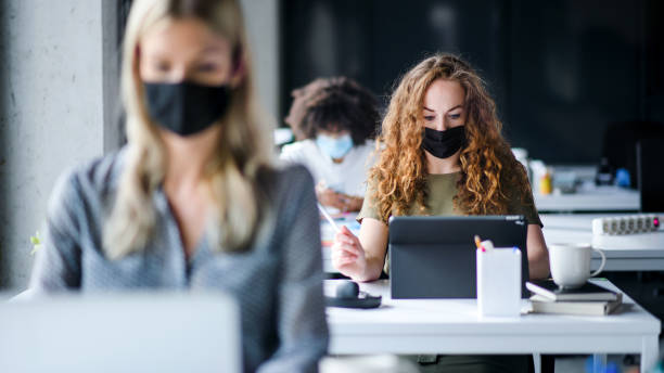 istock Young people with face masks back at work or school in office after lockdown. 1249880319