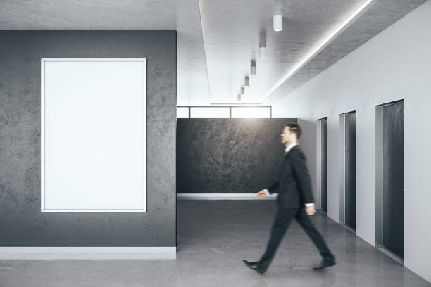 istock Businessman walking in minimalistic hall interior with blank banner on wall. 1249880431