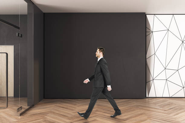 istock Businessman walking in office interior with copy space on wall 1249883406