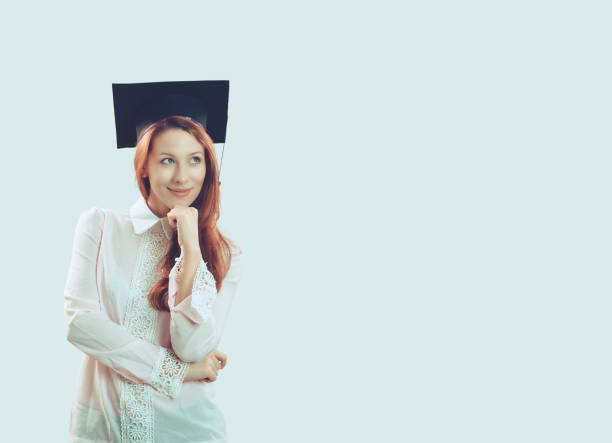 Portrait closeup young beautiful thoughtful graduate graduated student girl young woman in cap gown looking up thinking isolated light blue wall background. Graduation ceremony future career concept