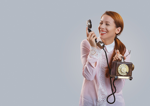 Happy redhead woman in pink shirt speaking on telephone and smiling at camera