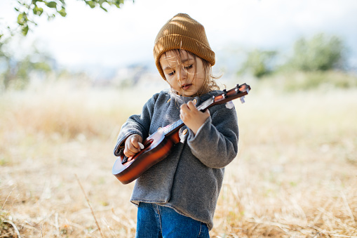 Adorable boy with guitar, standing on the grass. Toddler girl playing guitar at sunny countryside home garden