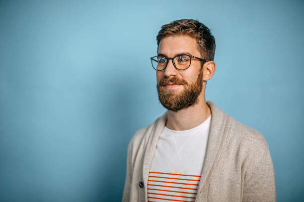 Studio shot of a young man looking sideways Studio shot of a young man looking sideways against blue background. nerd sweater stock pictures, royalty-free photos & images