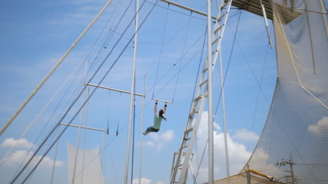 Young female trapeze artist flying in the sky