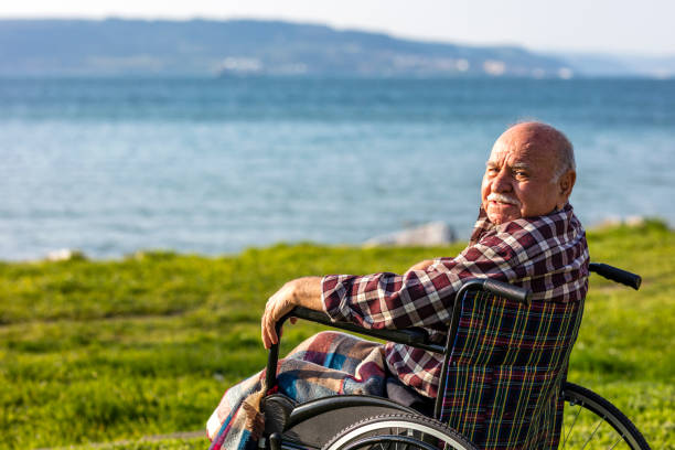 An adult Caucasian man with a physical disability and using a wheelchair takes the garbage can out to the side of a residential street in Oregon.