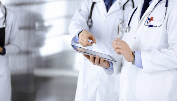 istock Group of unknown doctors use a computer tablet to check up some medical names records, while standing in a hospital office. Physicians ready to examine and help patients. Medical help, insurance in health care, best desease treatment and medicine concept 1249908542