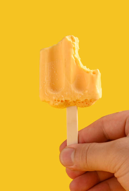istock hand holding a mostly eaten mango pudding flavor popsicle on a yellow background 1249908750