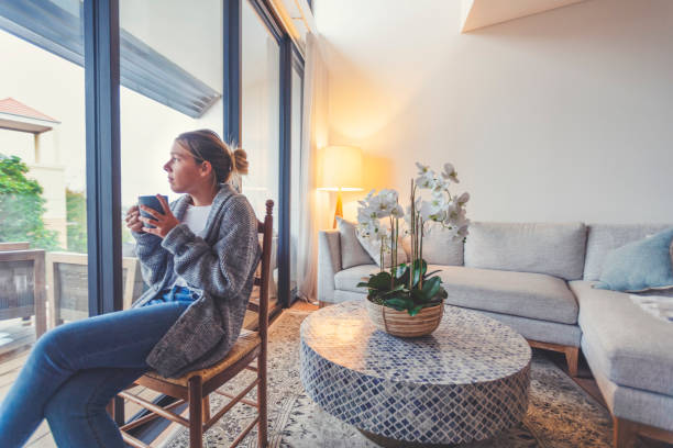 woman looking through the window drinking tea or coffee. - unemployment fear depression women imagens e fotografias de stock