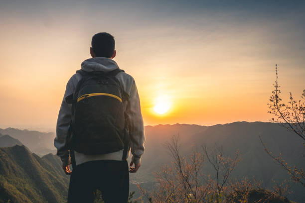istock Young man standing on top of mountain looking sunset 1249923499