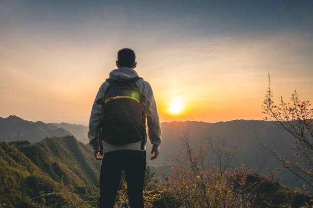 istock Young man standing on top of mountain looking sunset 1249923503