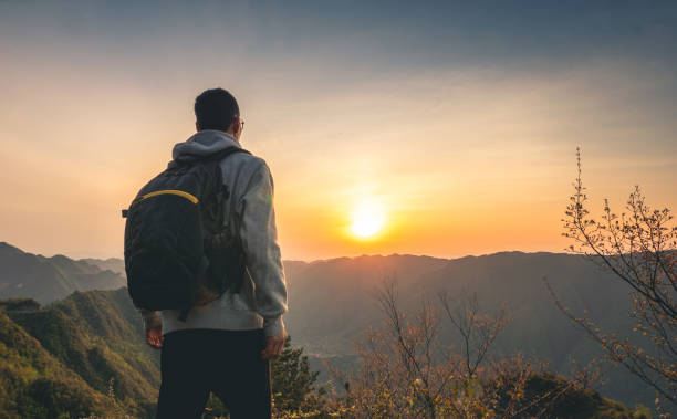 istock Young man standing on top of mountain looking sunset 1249923506