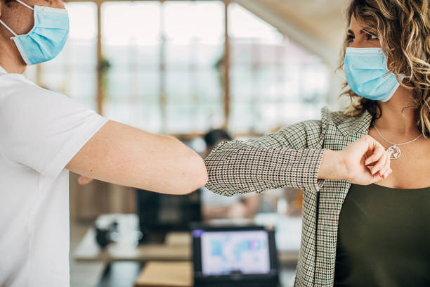 istock Man and woman with protective masks greeting with elbows in office 1249925783