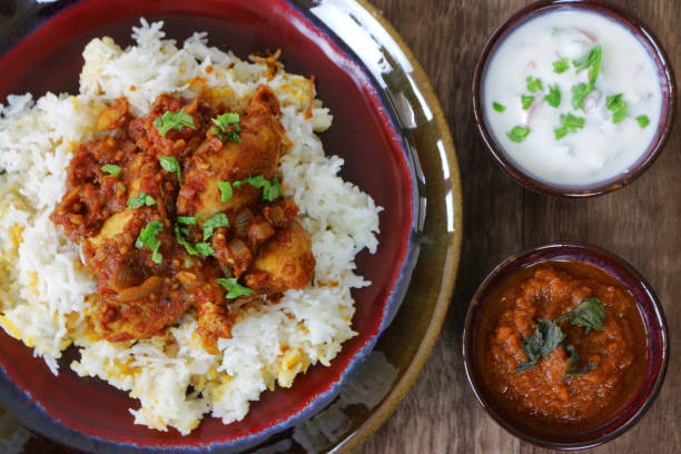 immagine di ciotola piena di biryani di pollo fatto in casa guarnita con foglie di coriandolo e servita con salsa tikka masala e raita (salsa a base di yogurt), vista elevata - herb plant rice white rice foto e immagini stock