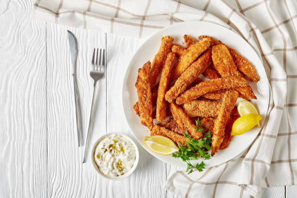 fish sticks, fish fillet fingers breaded and deep-fried fish sticks, fish fillet fingers breaded and deep-fried served on a white plate on a wooden table with tartar sauce and lemon wedges, horizontal view from above, flat lay free space fish stick stock pictures, royalty-free photos & images
