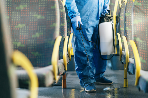 Public transportation healthcare. Man in protection suit disinfecting the bus interior, during COVID-19. Everything will be fine.