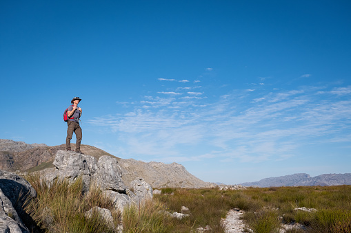 A male hiker with backpack stands on a rocky outcrop and admires the view. Male hiker enjoying nature and the outdoors.