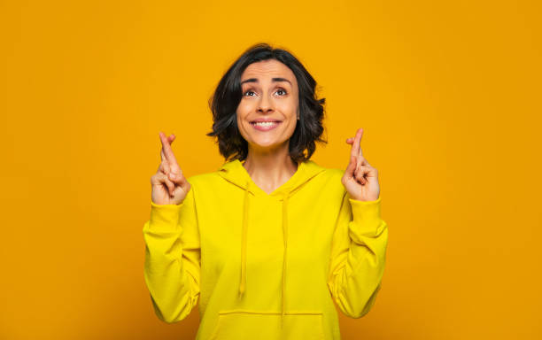 Things are going right! Close-up photo of excited beautiful girl dressed in a yellow hoodie, smiling and crossing her fingers, waiting for some lucky result while things are going right for her. Things are going right! Close-up photo of excited beautiful girl dressed in a yellow hoodie, smiling and crossing her fingers, waiting for some lucky result while things are going right for her. fingers crossed stock pictures, royalty-free photos & images